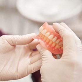 White-gloved hands holding complete set of dentures