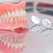 Full set of dentures on reflective surface next to dental mirror
