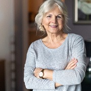 Senior woman in grey shirt smiling with arms folded