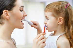 A woman and young girl brushing each other’s teeth.