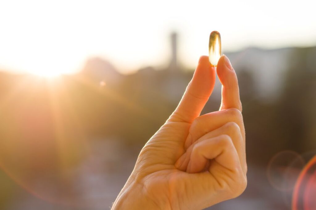 a hand holding a vitamin D gelcap in the sun